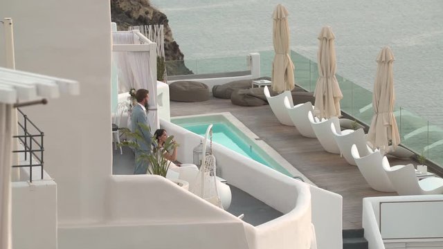 4k travel video luxury terrace of hotel in greece with swimmingpool, sun chairs and honeymoon couple in evening dress