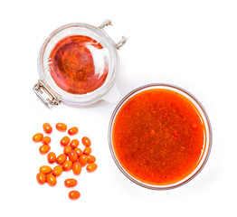 Fortified jam from fresh berries of sea buckthorn mashed with sugar in a glass jar, a vase with jam and berries