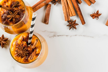 Traditional autumn dishes, spicy pumpkin pie smoothie with cinnamon, anise and oatmeal. In portioned glasses, on white marble table. Copy space top view