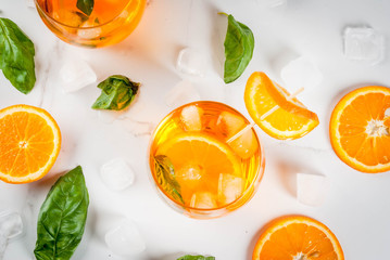 Summer refreshing drink, lemonade, cocktail with orange and basil. On a white marble table, copy...