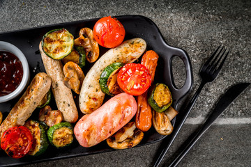Barbecue. Assortment of various grilled meat sausages, with vegetables BBQ - mushrooms, tomatoes, zucchini, onions. On a black stone table, on a black plate, with sauce. Copy space top view