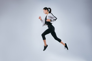 Fototapeta na wymiar Vertical image of sports woman running over gray background. Fitness young woman doing morning running.