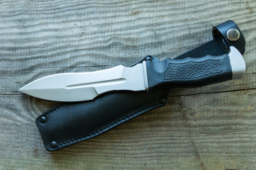 Army knife and black leather case. Wooden background.