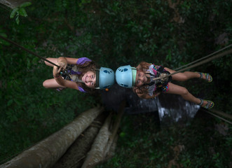 Two little girls rappelling from a tree, Thailand