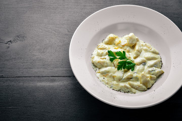 Dumpling from potatoes under cheese sauce. On a wooden background. Top view. Free space.