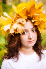 Naklejka na ściany i meble fall, beauty, femininity cincept. very cute caucasian young girl with delicate round face, big stunning brown eyes and nice curly hair, she is wearing autumnal wreath of yellow leaves of maple