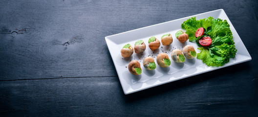French and Italian cuisine. Baked snails. On a wooden background. Top view. Free space.