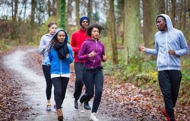 Fitness trainer guiding group of four determined young people during jogging in the forest