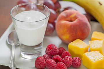 Close up of a plate with fruits and a glass of yogurt.