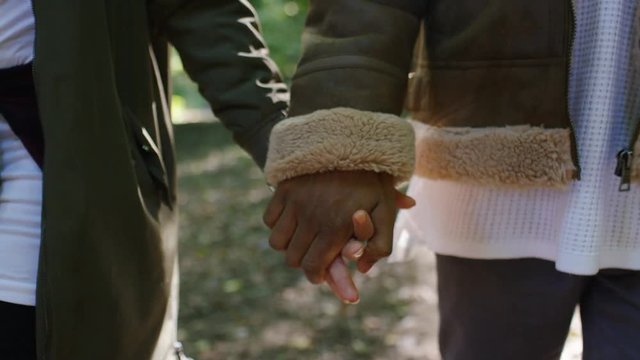Close up of a couple holding hands as they walk in a forest