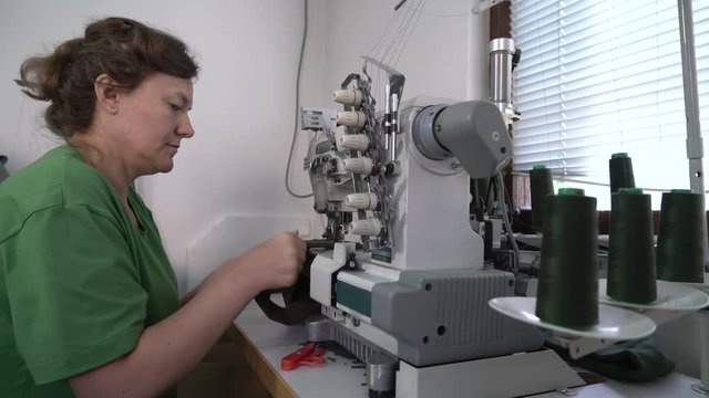 Middle close up Caucasian female person during sits at sewing machine and tailoring, dressmaker stitching cloth in workshop, interior scene