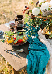 cutlery, picnic, romance concept. on the table in park there are few cups and glasses with tea, silver plate with rowan berries and orange persimmon, some ancient silverware