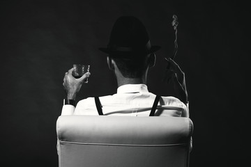 Fototapeta an unidentified man in a suit and hat with a cigar and whiskey staring into the distance. View from the back. The man is a mafia. Millionaire gangster businessman boss obraz