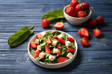 Plate with strawberry spinach salad on wooden table