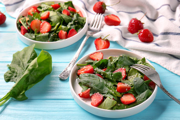 Plates with strawberry spinach salad on wooden table