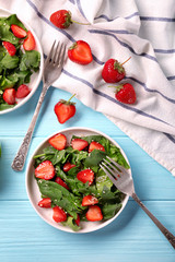 Plates with strawberry spinach salad on wooden table
