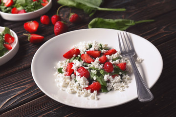 Plate with strawberry spinach salad on wooden table