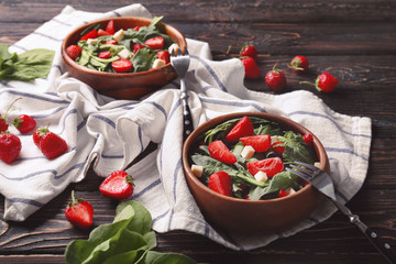 Bowls with strawberry spinach salad on wooden table