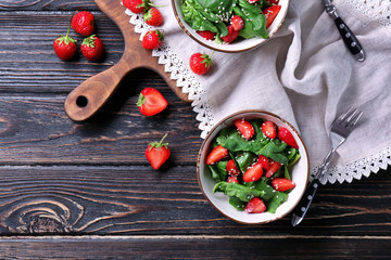 Bowls with strawberry spinach salad on wooden table
