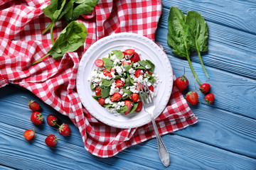 Plate with strawberry spinach salad on wooden table