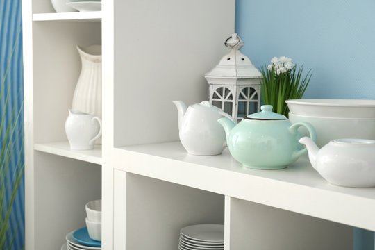 White storage stand with ceramic dishware near color wall
