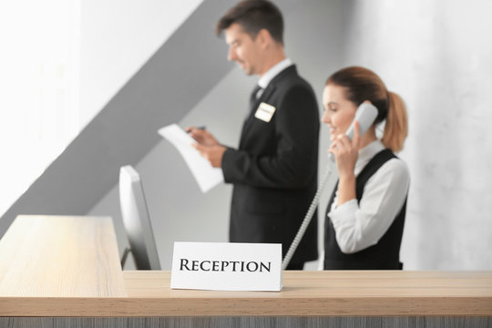 Reception sign and blurred workers at desk in hotel