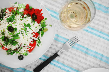 Glass of white wine and plate with exotic salad on striped cloth