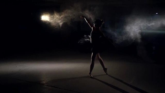 silhouette of dancing ballerina with hair in a bun, in huge empty gloomy hall