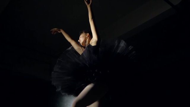 young pretty ballerina is wearing black dress is doing the ballet moves in darkness