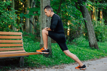 Male runner doing stretching exercise, preparing for morning workout in the park.