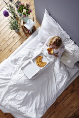 Fototapeta na wymiar red haired model eating pizza in bed white linen loft atmosphere
