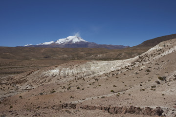 Eroded rock formations along Quebrada Chuba, a river valley high on the Altiplano of northern Chile in Lauca National Park. Snow capped peak of Volcano Guallatiri in the distance.