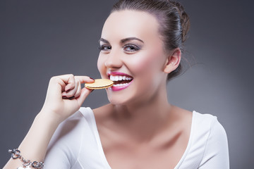 Food Concepts. Portrait of Young Smiling Happy Brunette Girl Eating Round Cookie. Demonstrating Enjoyment and Pleasure.Against Gray