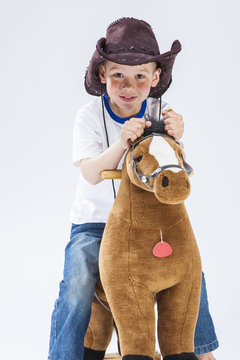 Natural Portrait of Happy Smiling and Glad Caucasian Little Boy in Cowboy Clothing With Symbolic Plush Horse Against White.