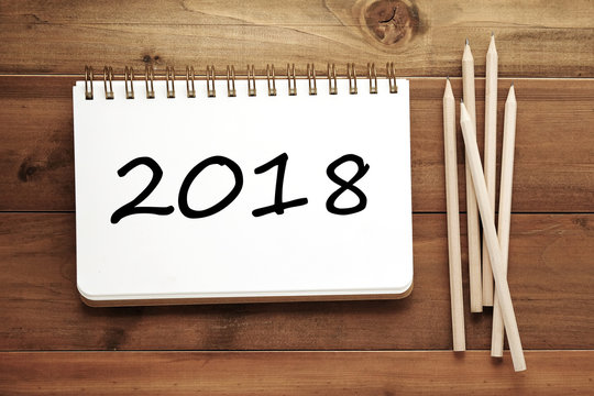 2018 on notebook paper and pencils on wood table background, new year banner concept