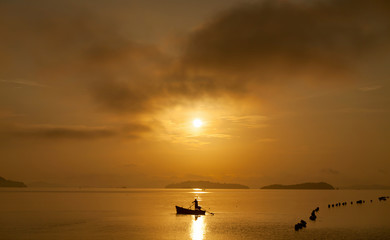Fisherman with a paddle in small boat at the tropical sea with beautiful sunrise or sunset in phuket thailand.