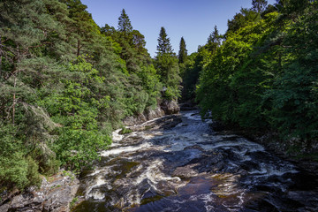 Summer view of a rushing stream, forest and small cottage in Invermoriston in the Scottish Highlands.