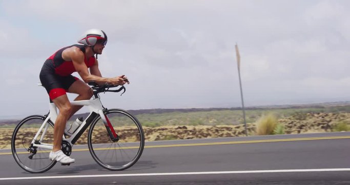 Triathlon biking - male triathlete cycling on triathlon bike. Fit man cyclist on professional triathlon bicycle wearing time trail helmet for ironman race. From Big Island Hawaii. SLOW MOTION RED EPIC