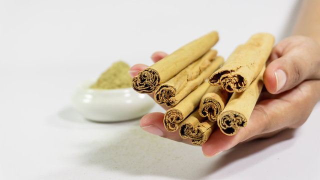 Hand holds cinnamon sticks and licorice powder on white background. health/ PCOS tretment