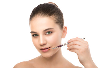 Fototapeta premium Portrait of beautiful young brunette woman with clean face. Beauty spa model girl with perfect fresh clean skin applying cosmetic brush. Youth and skin care concept. Isolated on a white background.