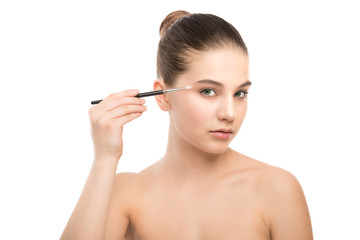 Fototapeta premium Portrait of beautiful young brunette woman with clean face. Beauty spa model girl with perfect fresh clean skin applying cosmetic brush. Youth and skin care concept. Isolated on a white background.