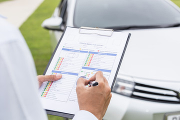 Asian car technician holding checklist paper in front of the car. For car repair concept