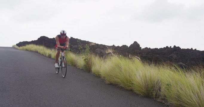 Triathlon cycling - male triathlete biking on triathlon bike. Fit man cyclist on professional triathlon bicycle wearing time trail helmet for ironman race. From Big Island Hawaii. SLOW MOTION RED EPIC