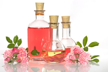 Obraz na płótnie Canvas Spa set with rose. rose petals oil , Perfumed Rose Water in glass bottles small pink roses with leaves on white background . Massage, aromatherapy and organic cosmetics concept