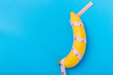 Yellow banana with measurement tape on blue background. Men penis size concept with empty free...
