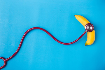 Stethoscope and yellow banana on blue background. For men penis check up concept. With empty free...