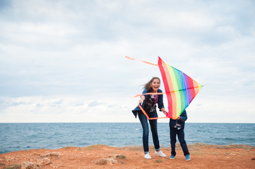 happy mother and child playing with a kite on the sea coast in the fall