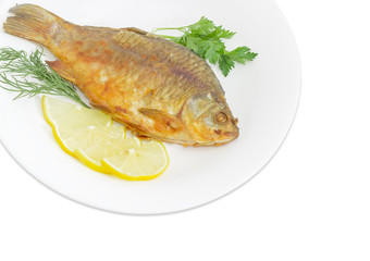 Fried crucian with lemon and potherb on white dish
