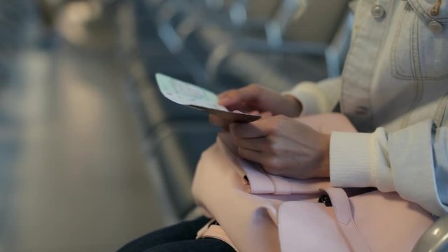 Close-Up. Girl With a Plane Ticket and a Phone Sits in the Airport Waiting Room