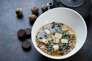 Miso soup with tofu cheese, wakame and sesame served in a white bowl, close-up